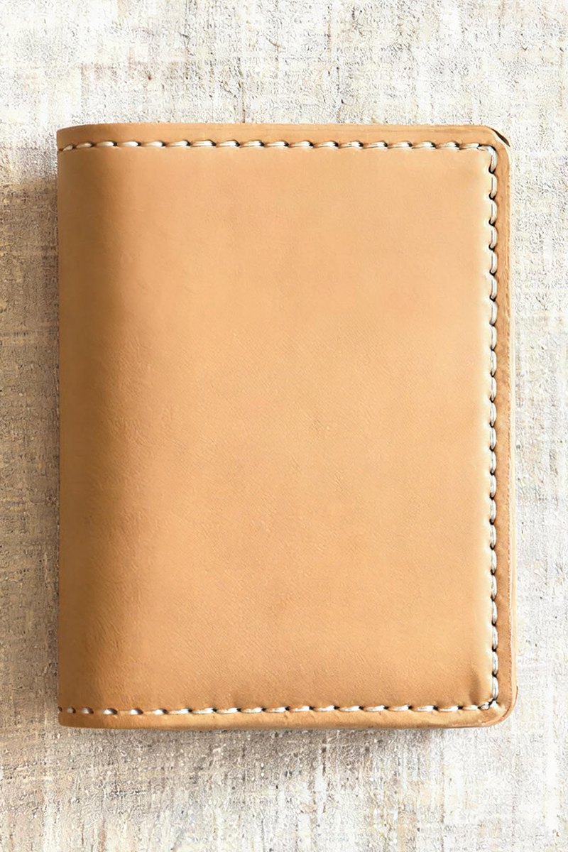 A tan leather wallet rests on linen with the stitching clearly visible.