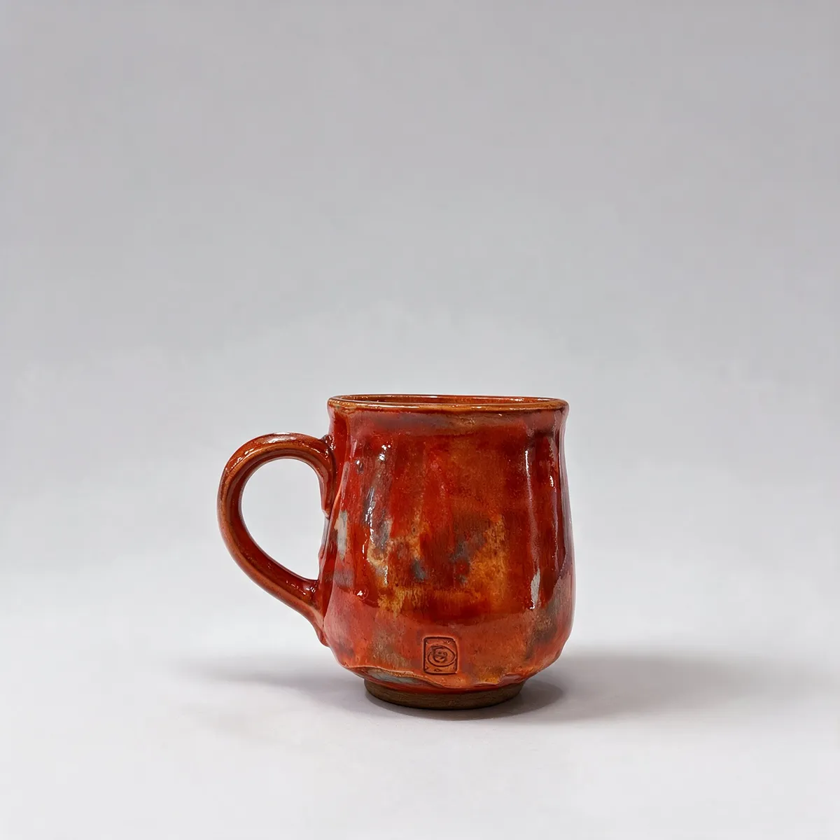 A red glazed ceramic mug sits against a light-gray backdrop.