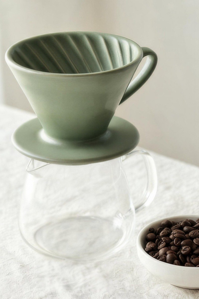 A sage-green ceramic coffee dripper sits on a clear glass server.